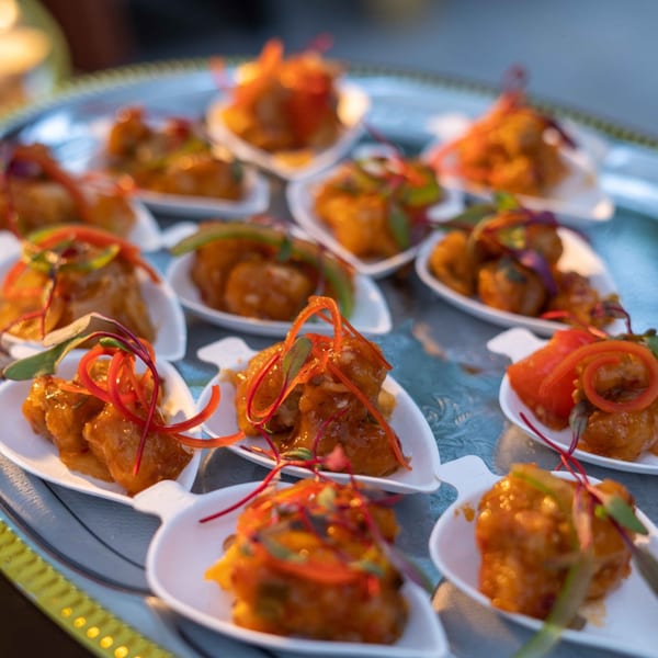 A silver tray holds multiple small white dishes of Indian appetizers, garnished with red and green peppers.