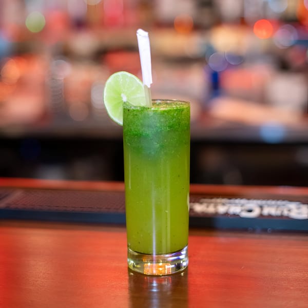 A tall glass of green Indian mint mojito with a lime wedge and straw on a bar.