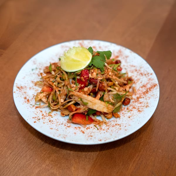 Indian salad with noodles, vegetables, peanuts, and a lime wedge on a white plate.