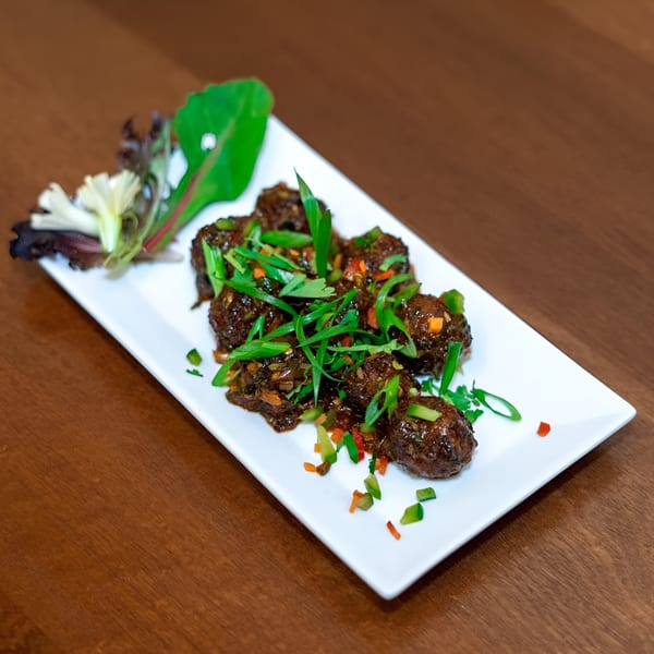 Indian Manchurian dish, featuring dark brown meatballs garnished with green onions and colorful diced vegetables.
