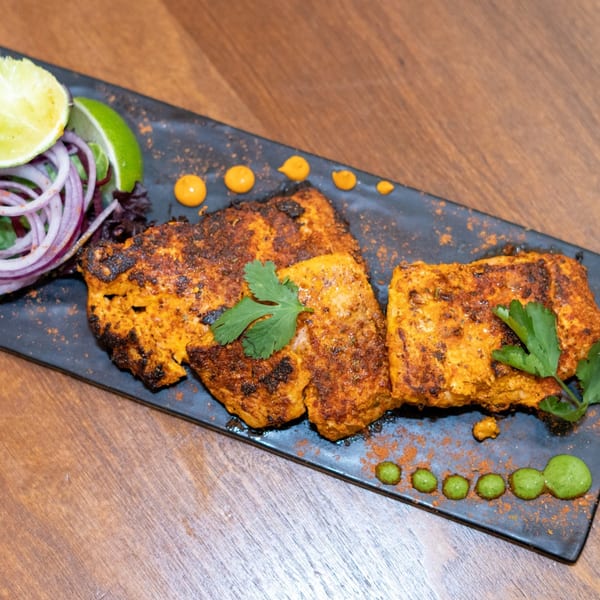 Indian paneer tikka, garnished with cilantro, red onions, and lime, on a black platter.