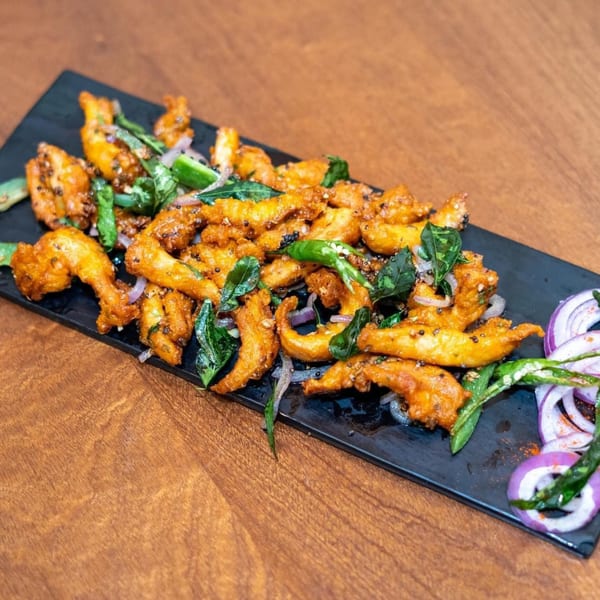 Crispy fried Indian chicken pakora or shrimp pakora, garnished with curry leaves, green chilies, and red onions.