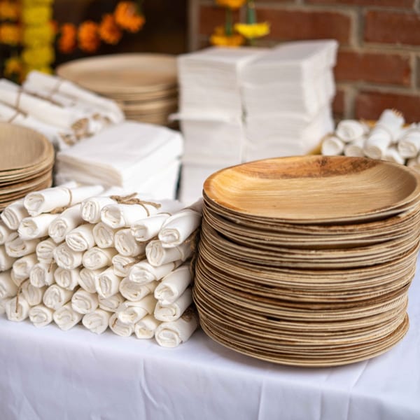 Stacks of eco-friendly plates and rolled napkins on a white tablecloth, ready for an Indian meal.