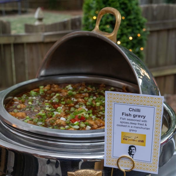 A chafing dish of The Yellow Chilli's Indian Chilli Fish Gravy, garnished with green onions.