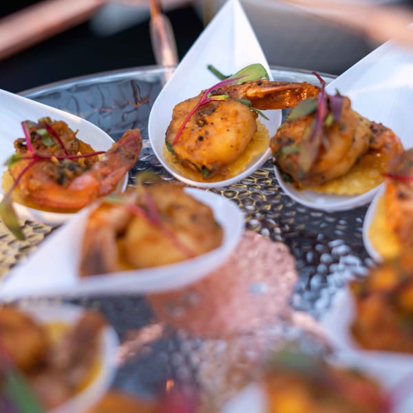 Close-up of Indian-spiced shrimp appetizers in white, teardrop-shaped dishes on a glass tray.