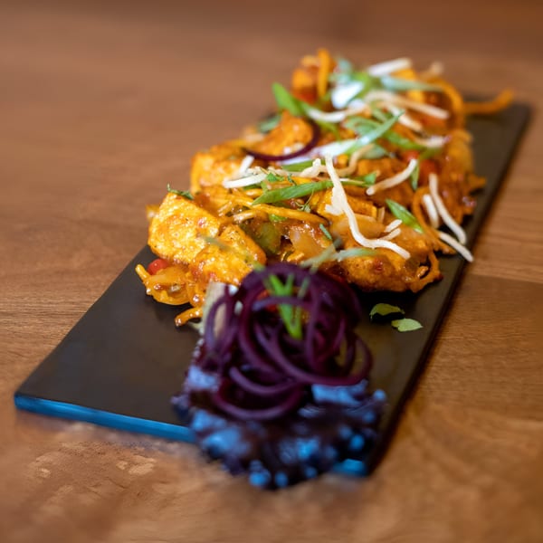 Indian chili paneer, garnished with shredded onions and green herbs, on a black rectangular plate.