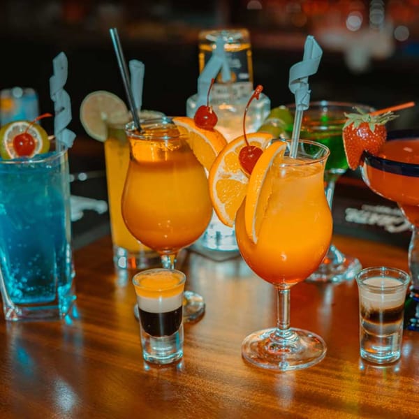 A variety of colorful cocktails and shots, garnished with fruit, on a wooden bar.