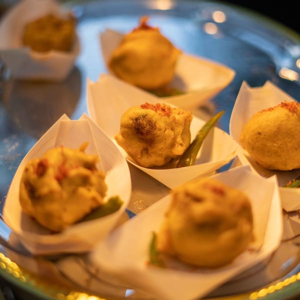 A close-up of several Indian vada pav appetizers in white paper cups on a silver tray.