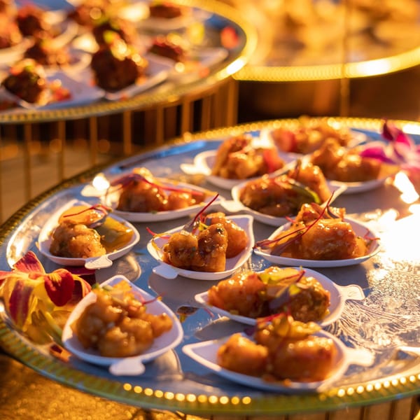 Indian appetizers, small portions of chicken in sauce, on a silver platter with orchids.